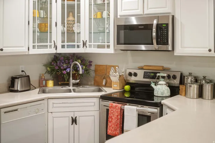 Kitchen featuring white cabinets, stainless steel appliances, light countertops, and glass fronted cabinets