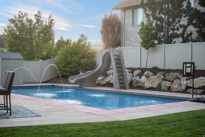View of pool featuring a water slide, a fenced backyard, a storage shed, and patio surround