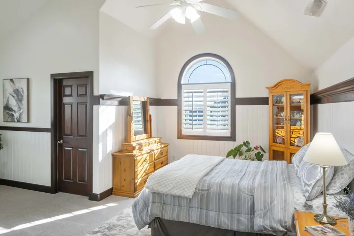 Bedroom featuring a wainscoted wall, lofted ceiling, light carpet, ceiling fan, and wooden walls