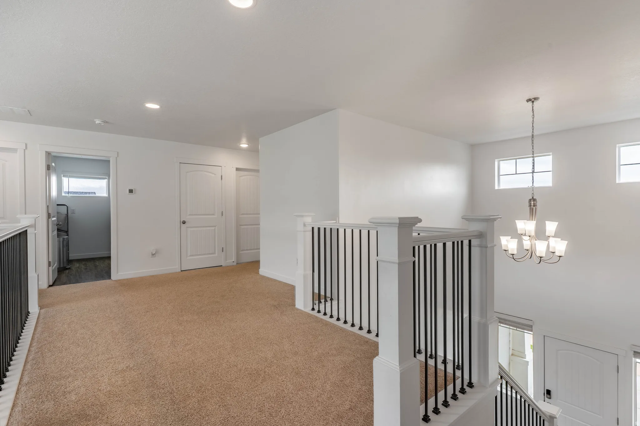Hallway with an upstairs landing, light colored carpet, and a chandelier