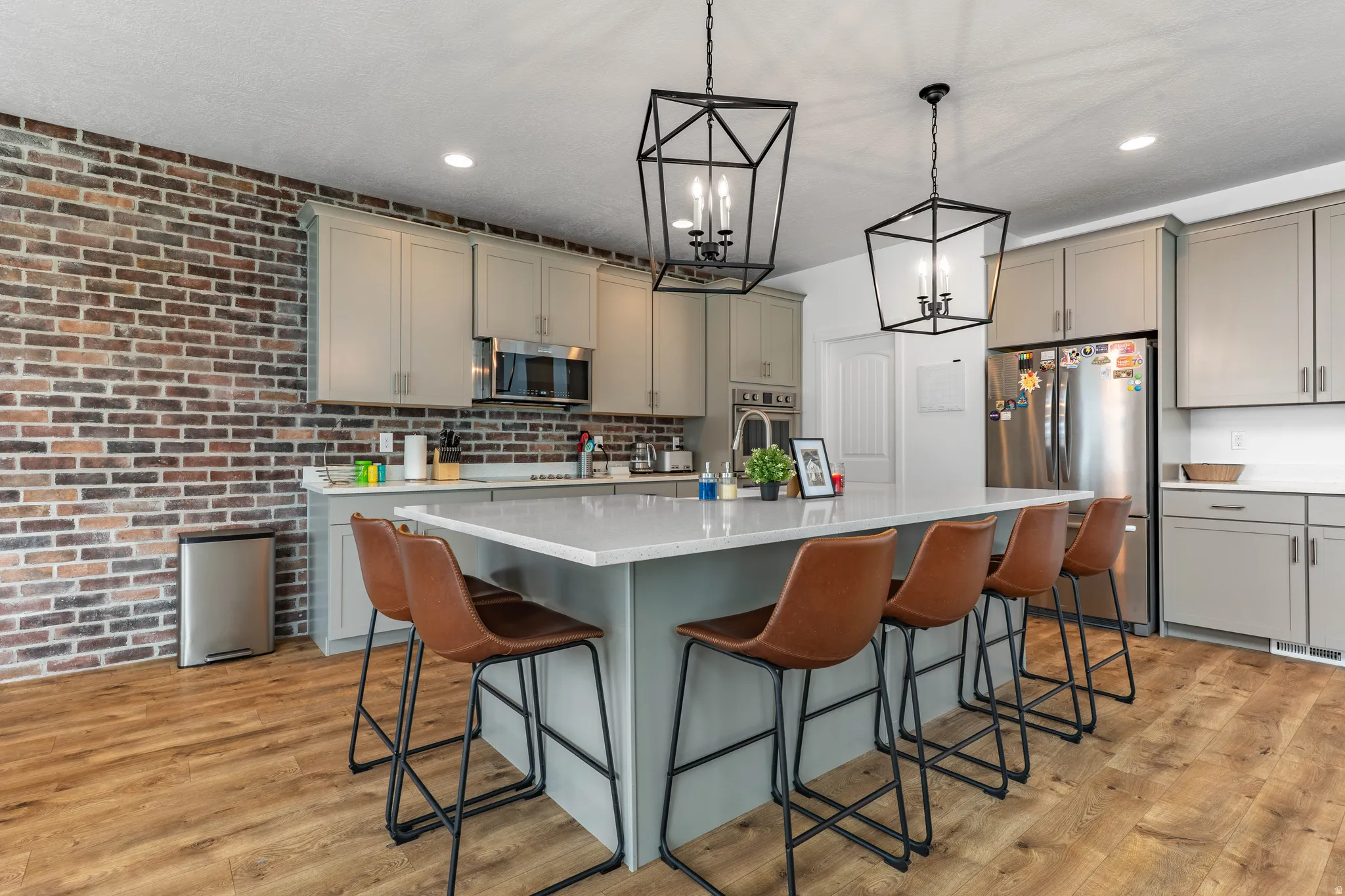 Kitchen with stainless steel appliances, a breakfast bar, gray cabinets, brick wall, and a kitchen island with sink