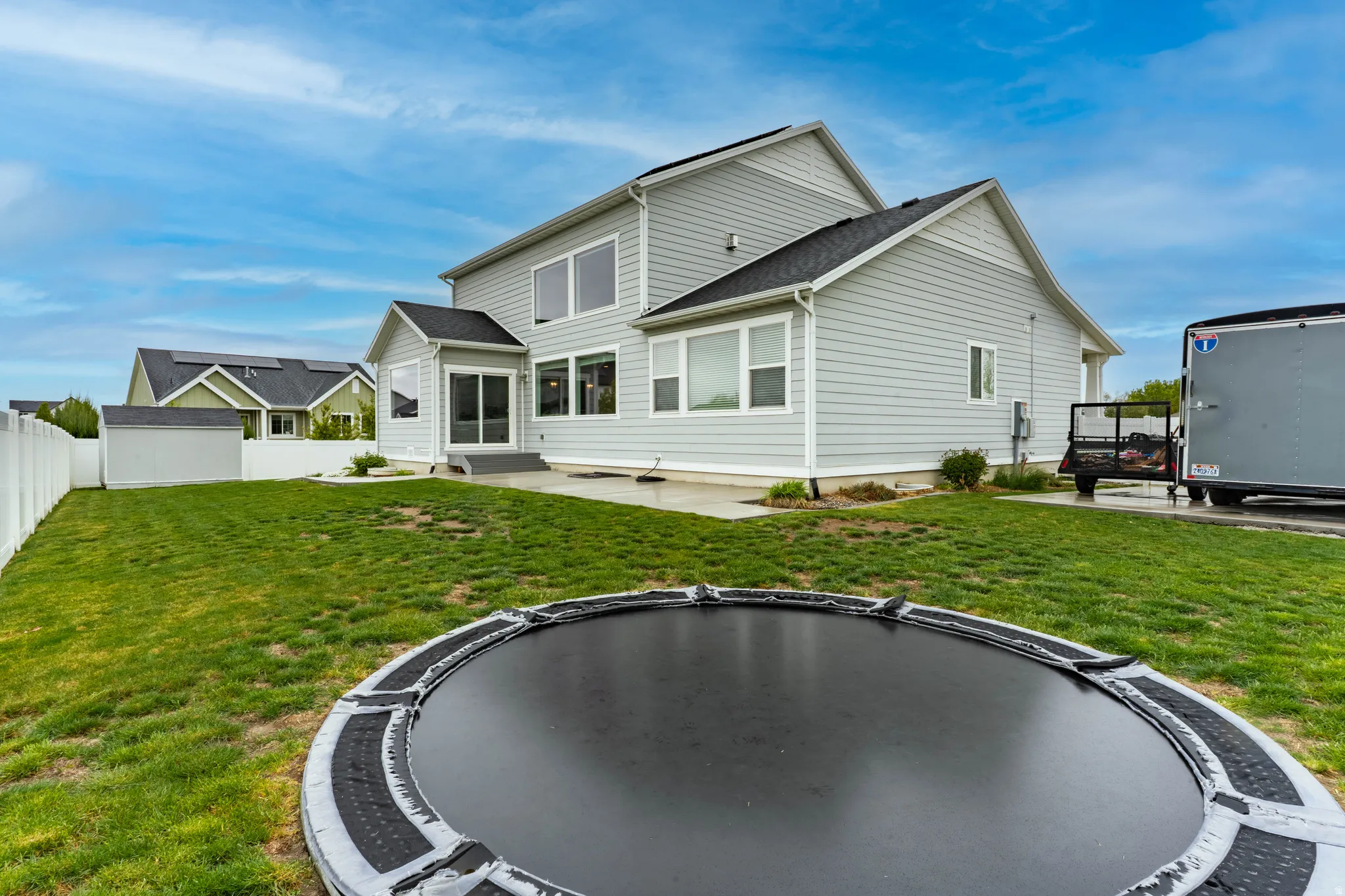 Rear view of house featuring a trampoline, a patio, and a shingled roof