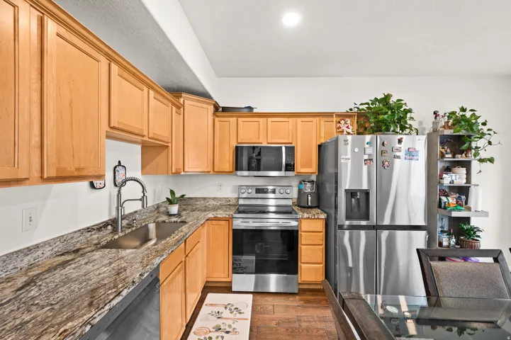 Kitchen with stainless steel appliances, dark stone counters, light wood finish cabinetry, and dark wood-type flooring