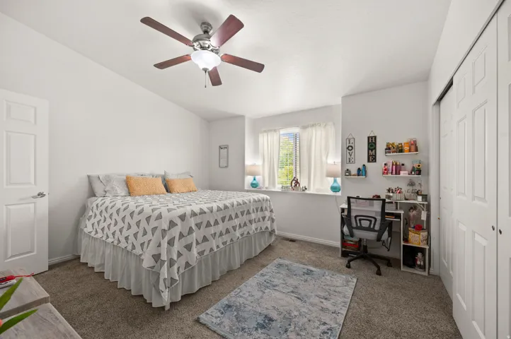 Bedroom with a closet, dark colored carpet, ceiling fan, and a desk