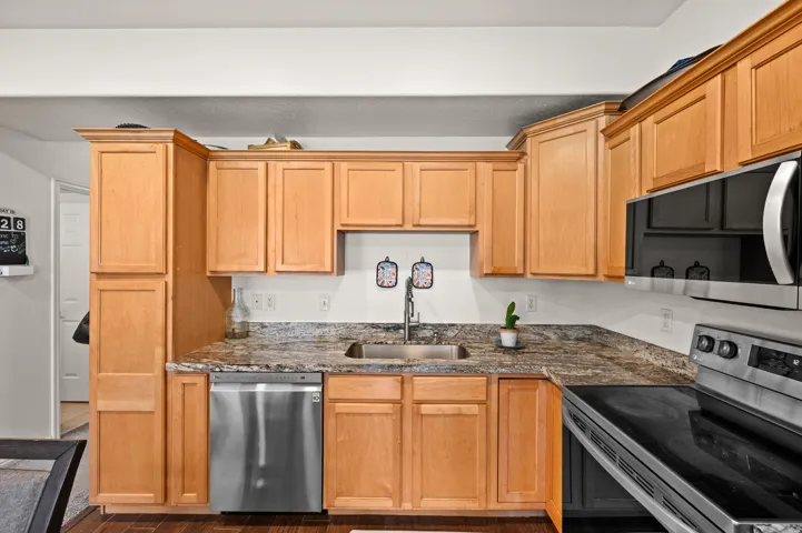 Kitchen with stainless steel appliances, dark wood-style floors, and dark stone counters