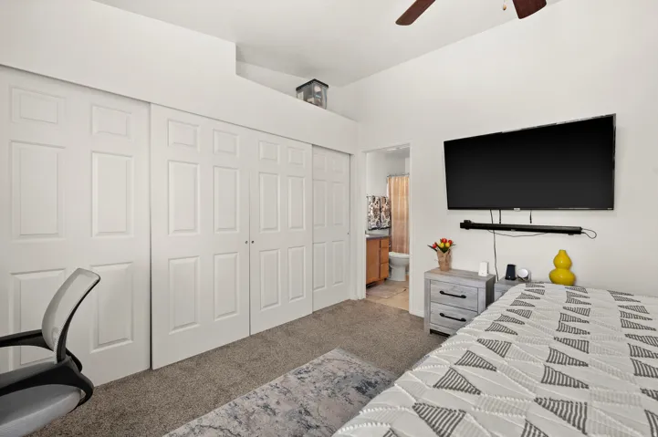 Bedroom featuring light carpet, a closet, connected bathroom, and a ceiling fan