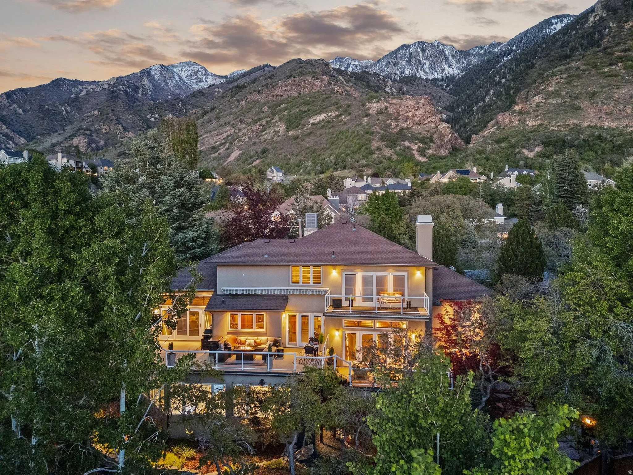 Back of house at dusk featuring stucco siding, a balcony, a chimney, and a mountain view