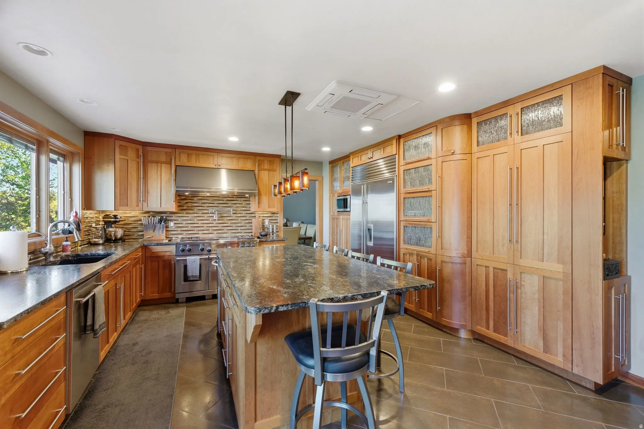 Kitchen featuring high end appliances, a kitchen breakfast bar, a center island, glass insert cabinets, and pendant lighting