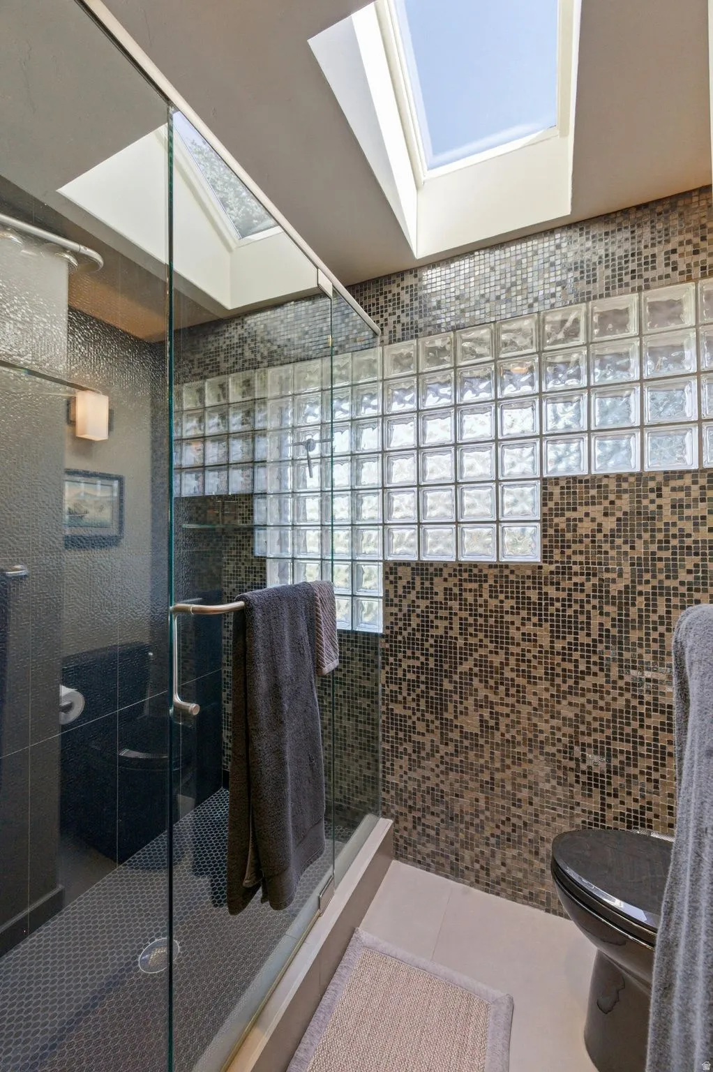 Full bathroom featuring light tile patterned floors, a stall shower, tile walls, and a skylight