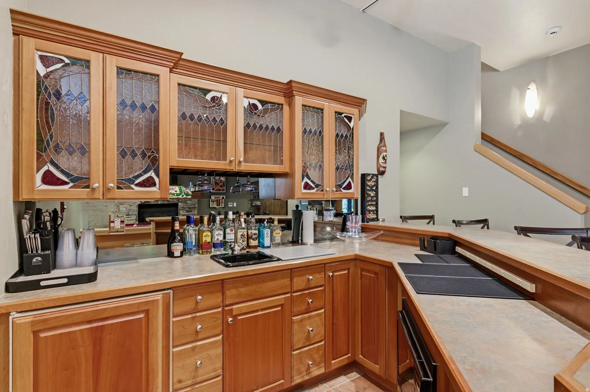 Bar featuring light countertops, wood finish cabinets, wall oven, and glass insert cabinets
