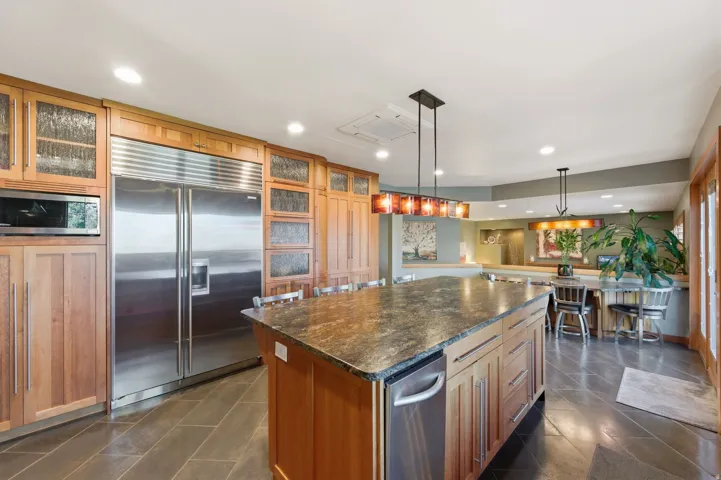 Kitchen featuring glass fronted cabinets, stainless steel appliances, hanging light fixtures, and a center island