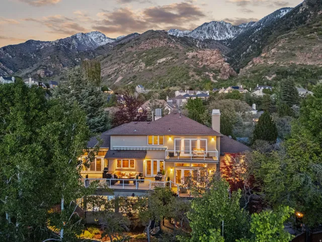 Back of house at dusk featuring stucco siding, a balcony, a chimney, and a mountain view