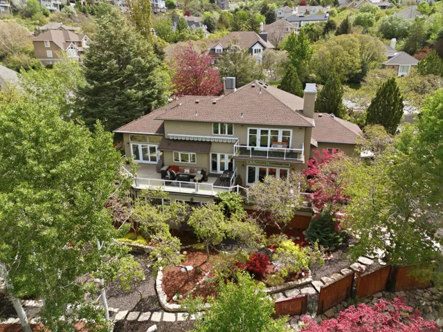 Back of property featuring a chimney, a shingled roof, stucco siding, a balcony, and view of wooded area