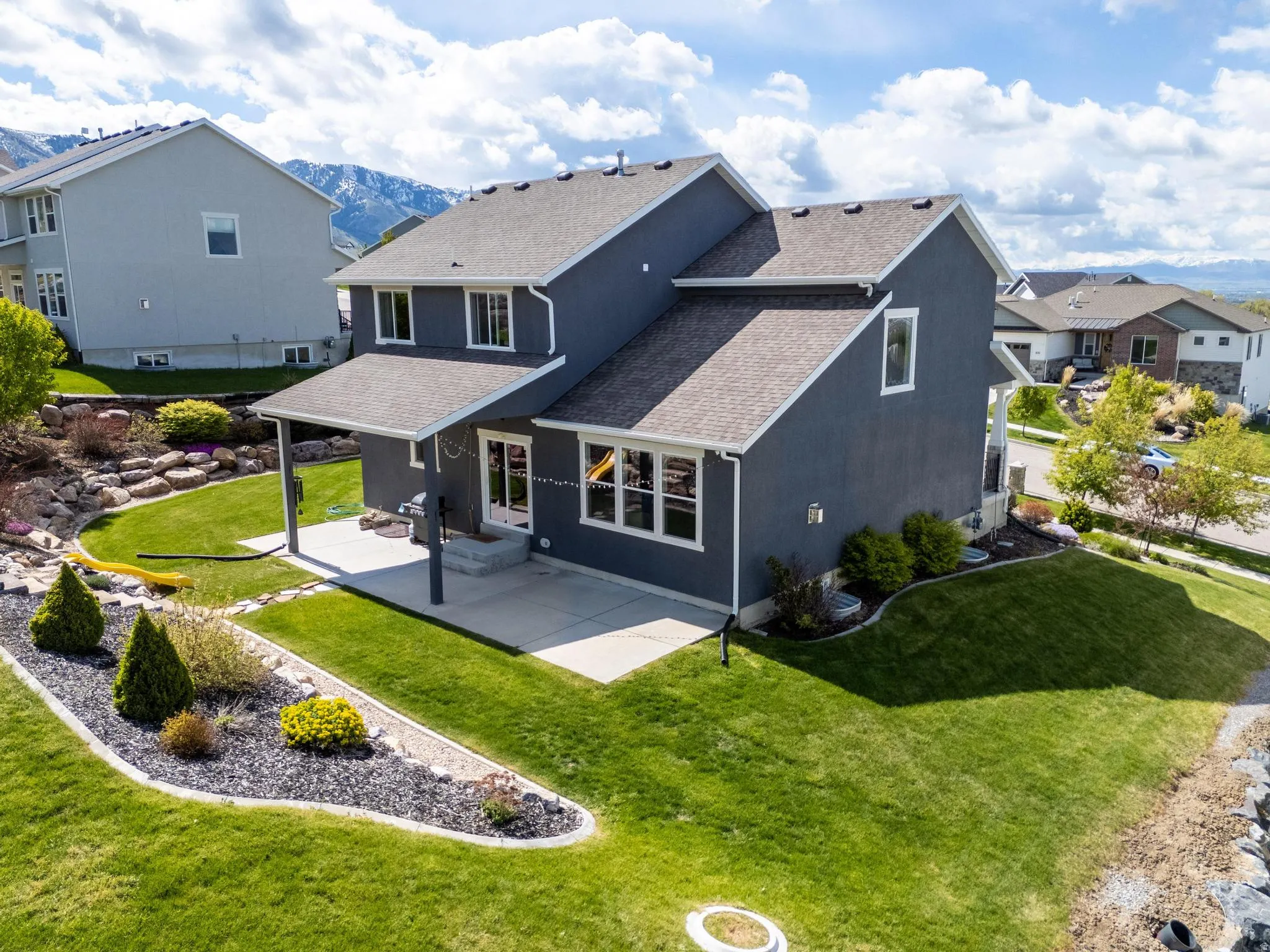 Rear view of house featuring roof with shingles, a yard, a patio area, a residential view, and a mountain view