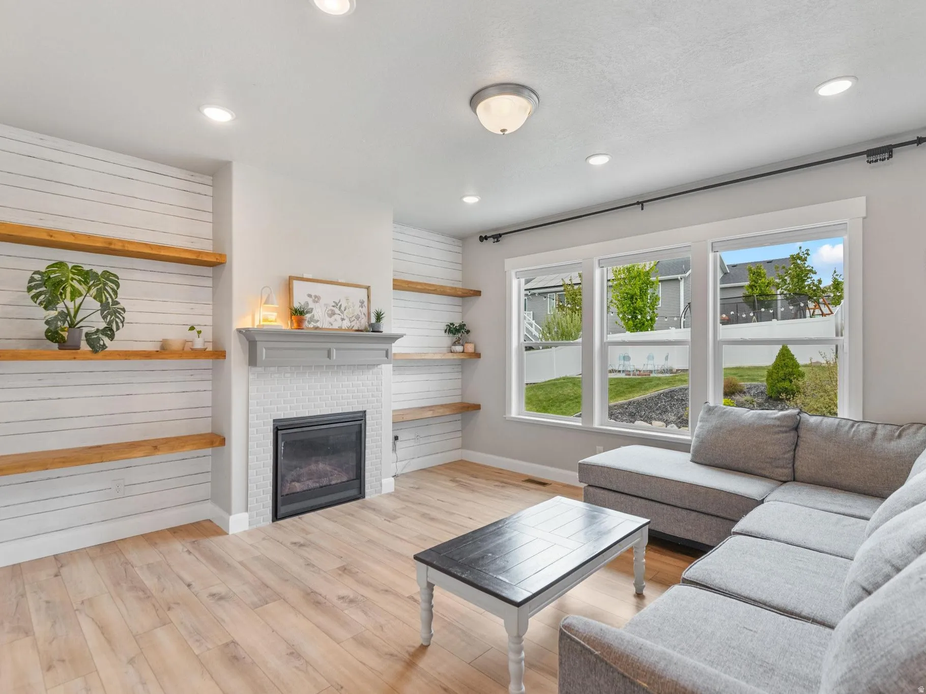 Living room featuring light wood finished floors, a glass covered fireplace, and recessed lighting