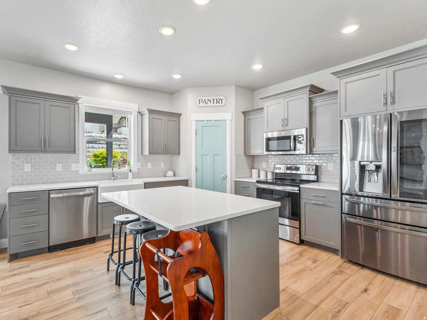 Kitchen featuring gray cabinetry, stainless steel appliances, light wood finished floors, a breakfast bar area, and a kitchen island