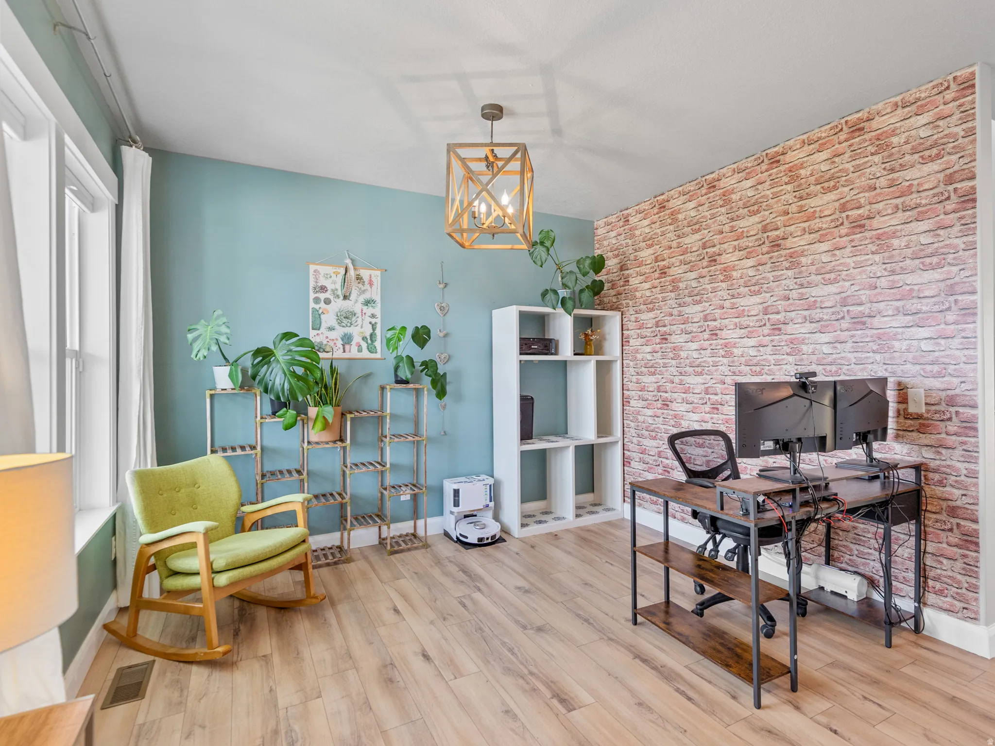 Home office featuring light wood-type flooring, suspended lighting, brick wall, and an accent wall