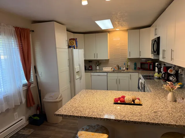 Kitchen with baseboard heating, light stone countertops, white cabinets, a peninsula, and a breakfast bar