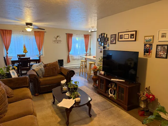 Living room featuring a textured ceiling, a ceiling fan, a baseboard heating unit, and light wood-type flooring