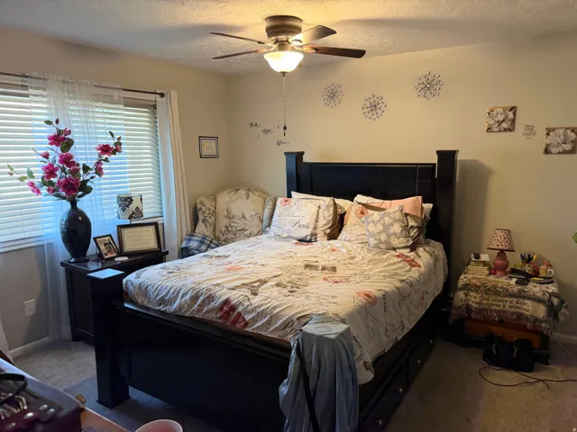Bedroom with a textured ceiling, carpet, and a ceiling fan