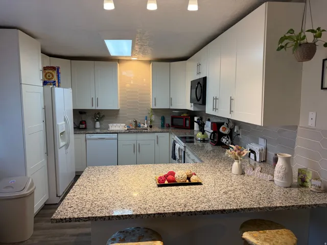 Kitchen featuring decorative backsplash, light stone countertops, white appliances, and white cabinetry