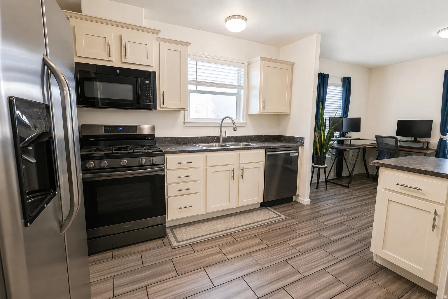 Kitchen with dark countertops, stainless steel appliances, wood finish floors, a desk, and healthy amount of natural light