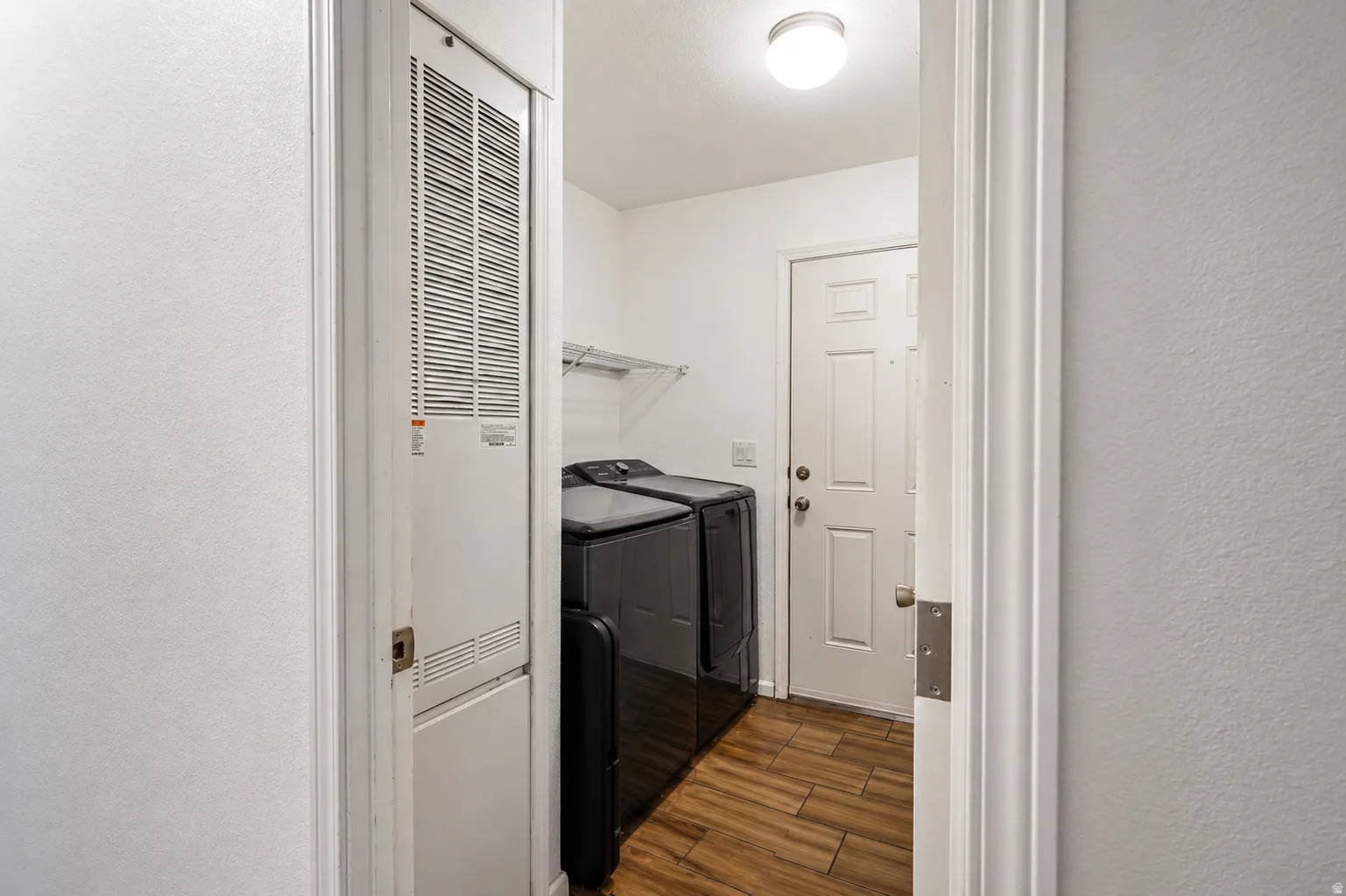 Laundry room featuring a textured wall, dark wood-style floors, separate washer and dryer, and a heating unit