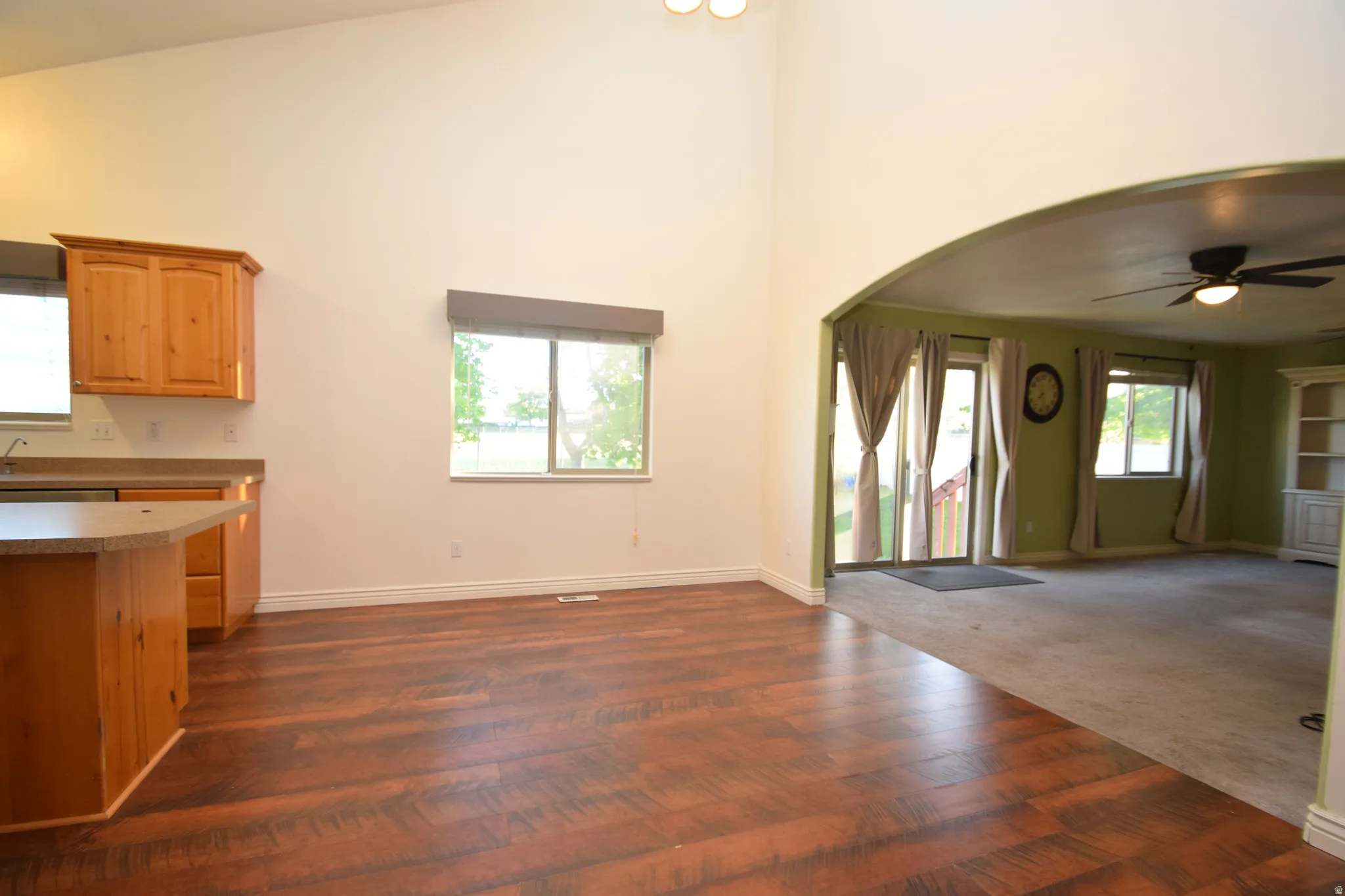 Kitchen with open floor plan, a ceiling fan, arched walkways, dark wood-style floors, and lofted ceiling