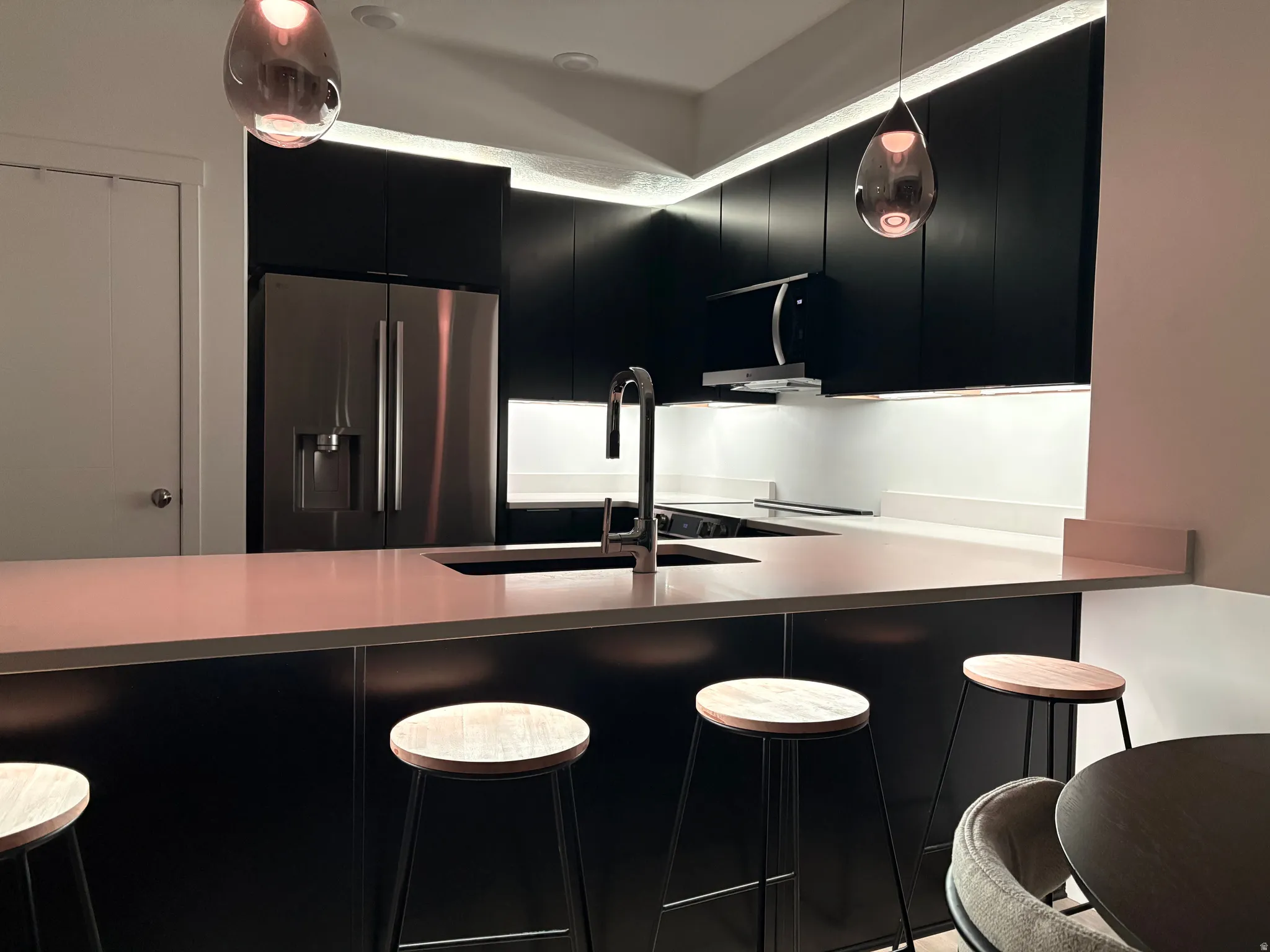 Kitchen with dark cabinetry, a kitchen breakfast bar, stainless steel refrigerator with ice dispenser, modern cabinets, and decorative light fixtures