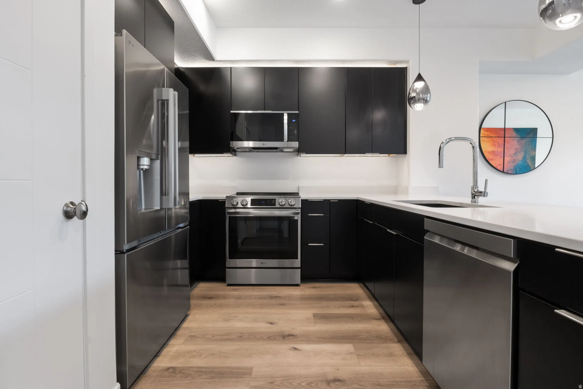 Kitchen featuring dark cabinetry, stainless steel appliances, modern cabinets, light stone countertops, and light wood-style flooring