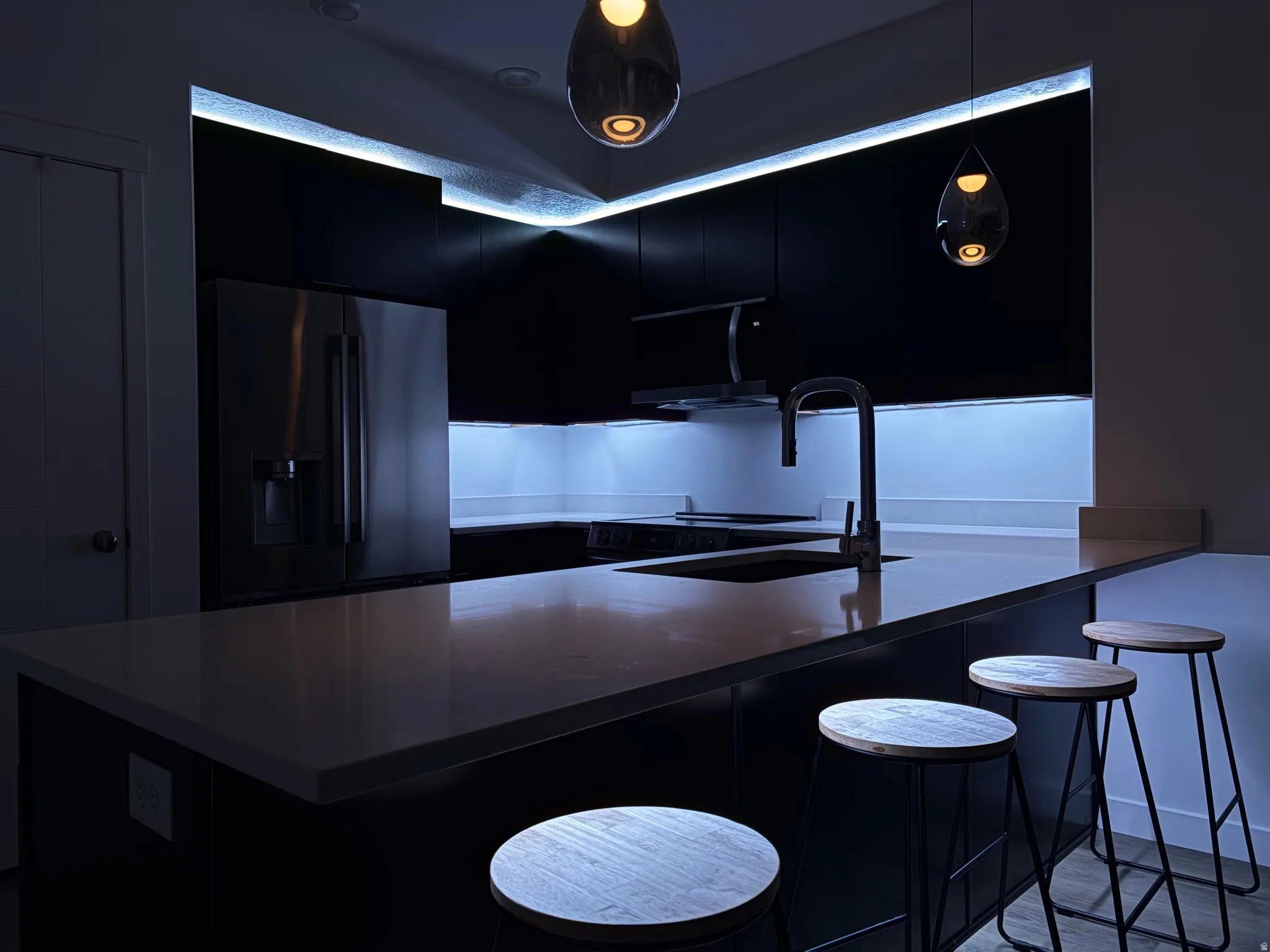 Kitchen featuring dark cabinets, a breakfast bar area, fridge with ice dispenser, and a peninsula