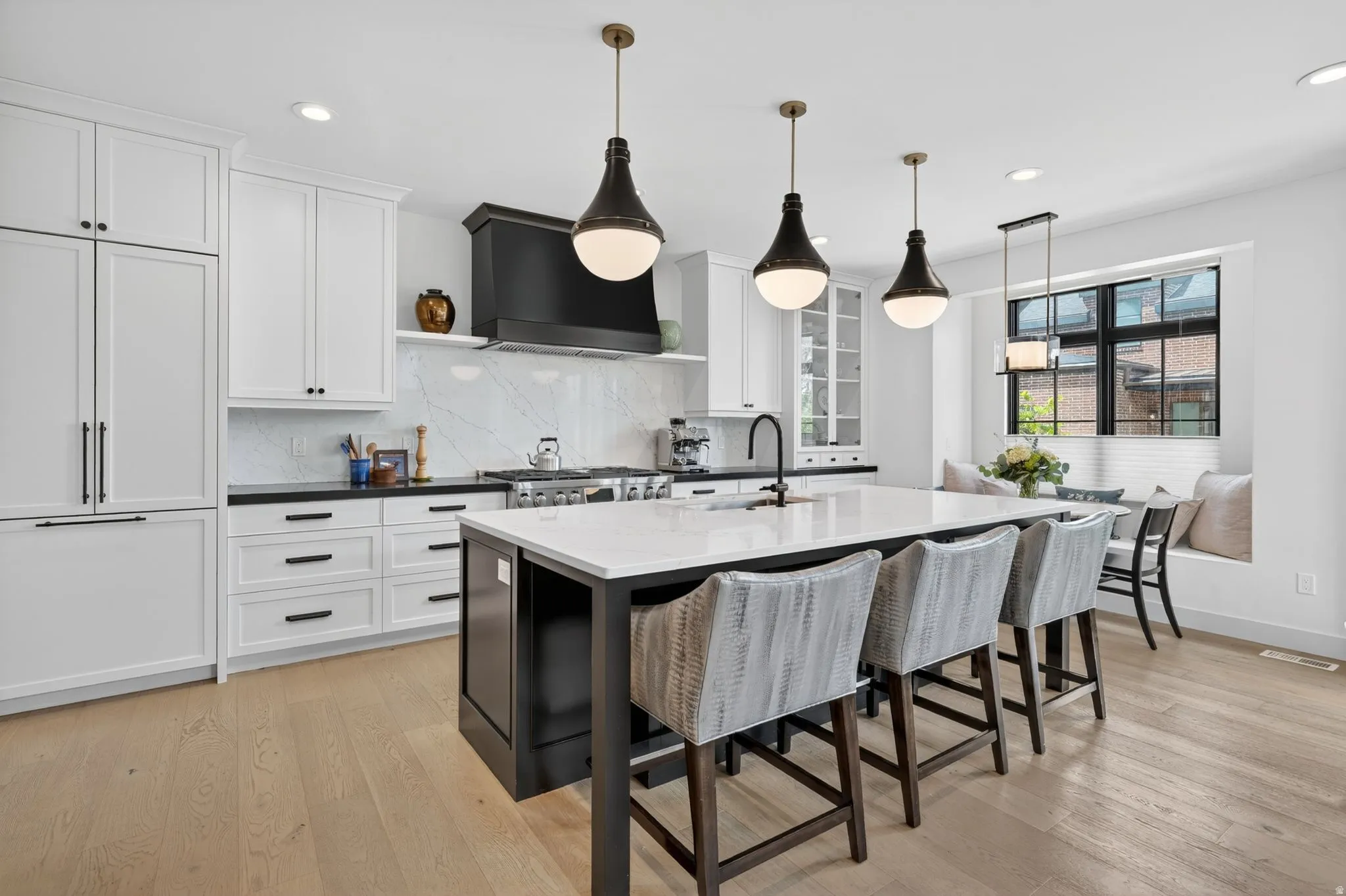 Dual tone kitchen with a breakfast bar area, an island with sink, decorative backsplash, light wood-style flooring, and pendant lighting