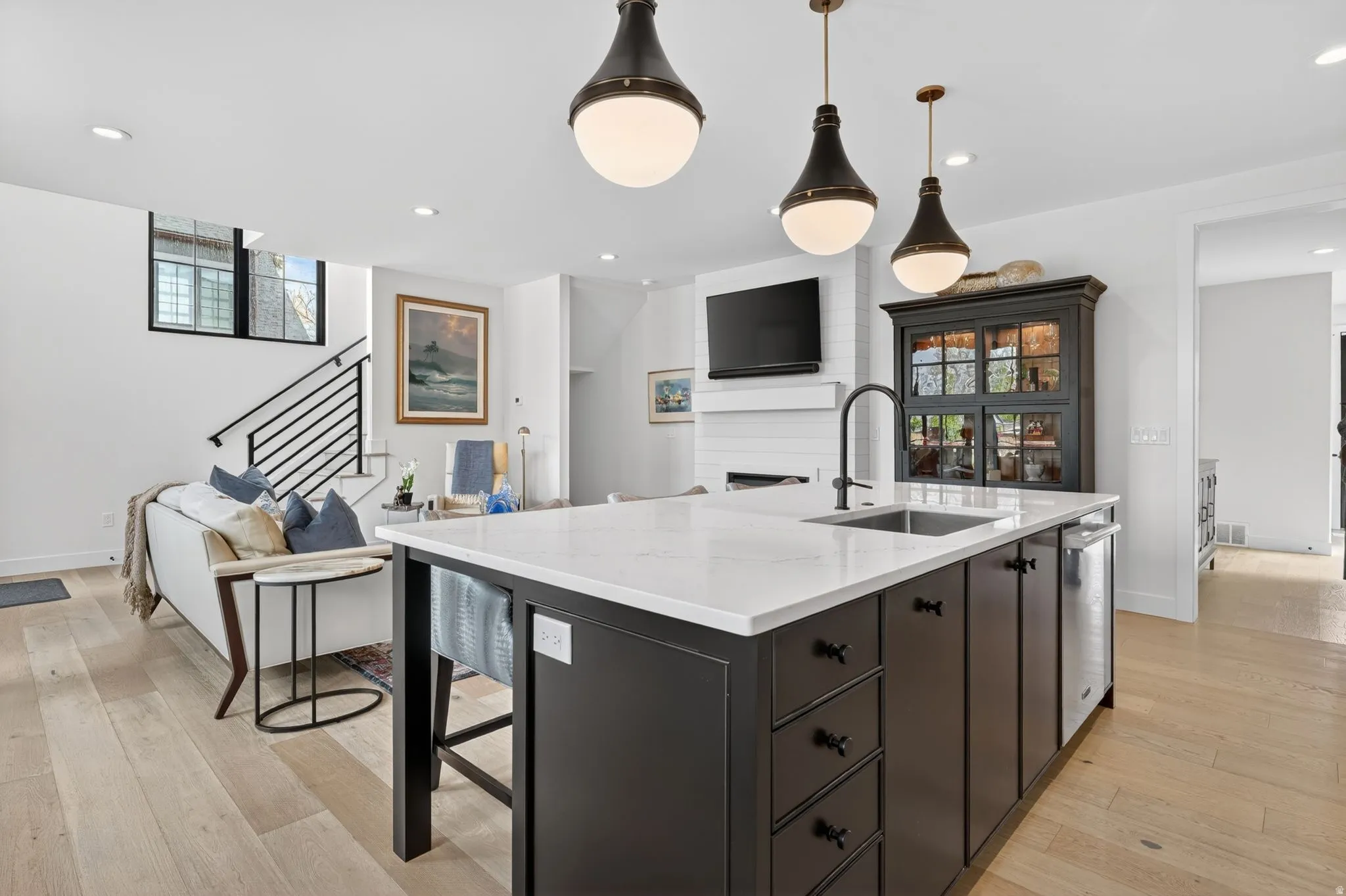 Kitchen featuring open floor plan, a center island with sink, light stone countertops, light wood-style flooring, and hanging light fixtures