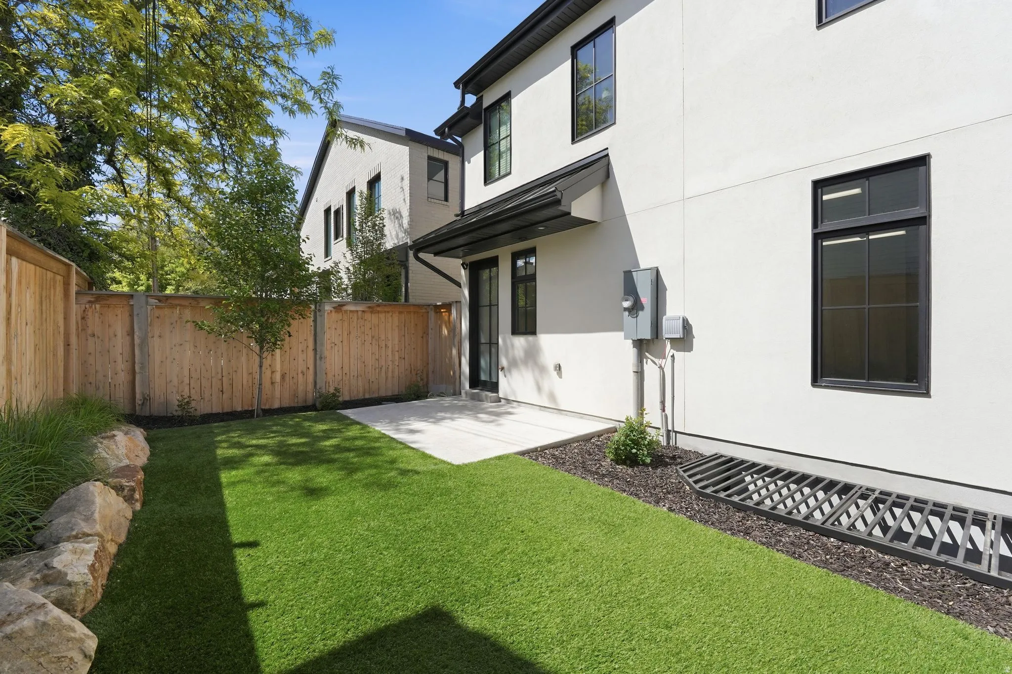 Rear view of house with stucco siding, a fenced backyard, synthetic turf, and a patio