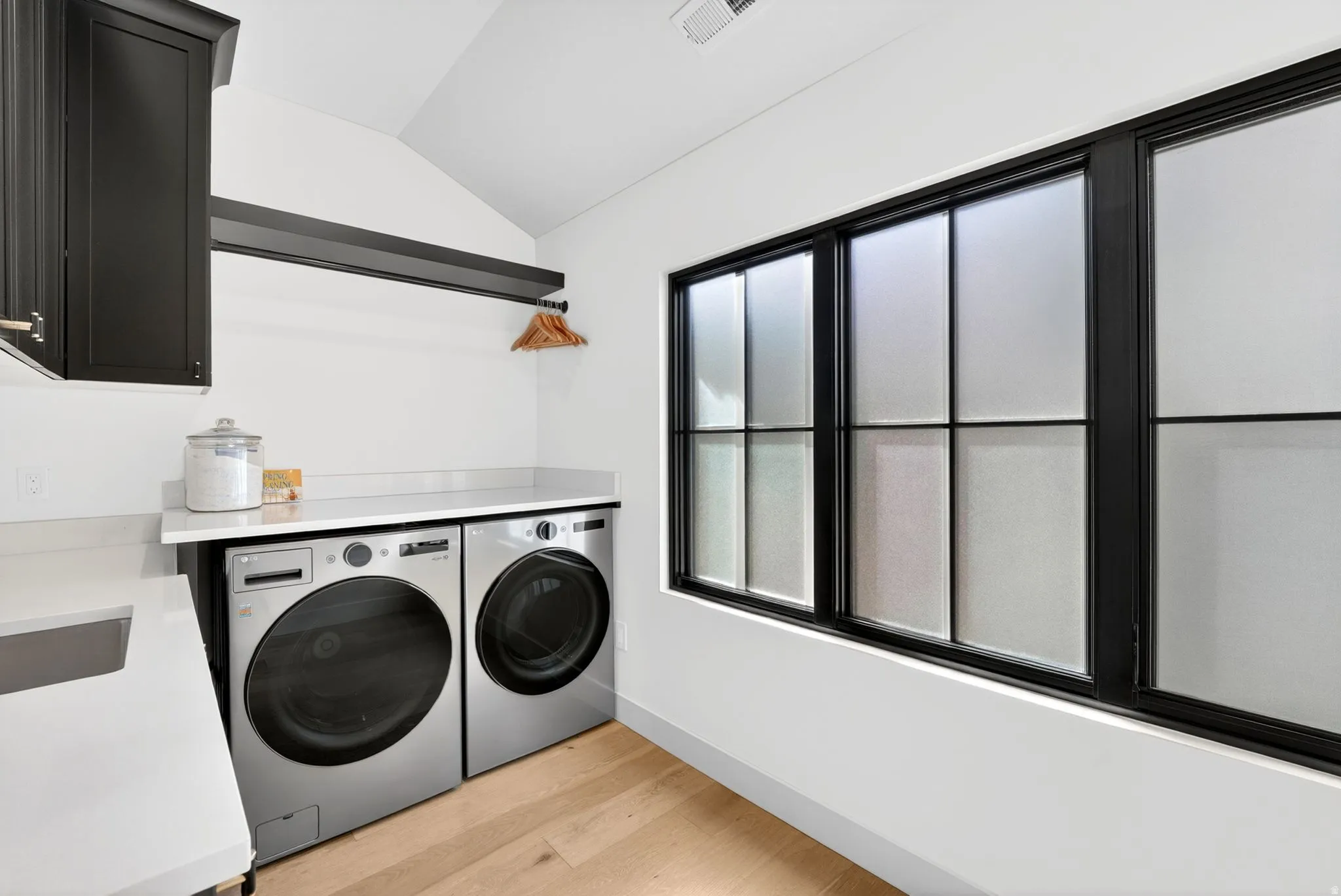 Laundry area with light wood-style flooring, washing machine and clothes dryer, lofted ceiling, and cabinet space