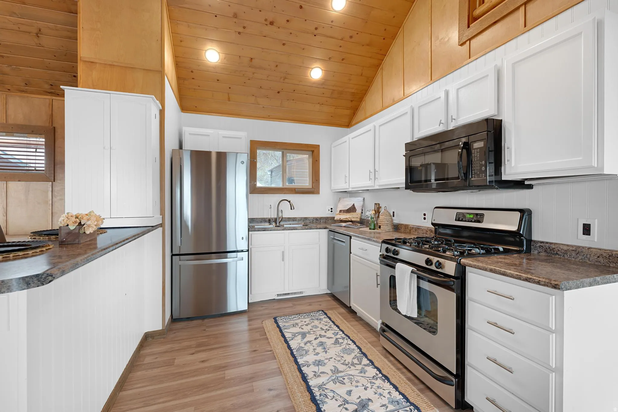 Kitchen with dark countertops, stainless steel appliances, recessed lighting, white cabinetry, and a vaulted wood ceiling