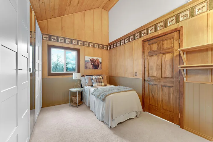 Bedroom featuring lofted ceiling, light colored carpet, wood walls, and wainscoting
