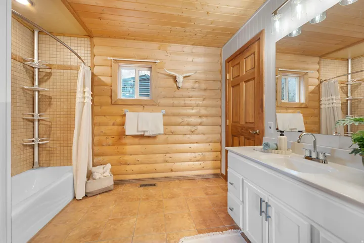 Full bathroom featuring wood ceiling, log walls, vanity, and shower / bath combo with shower curtain