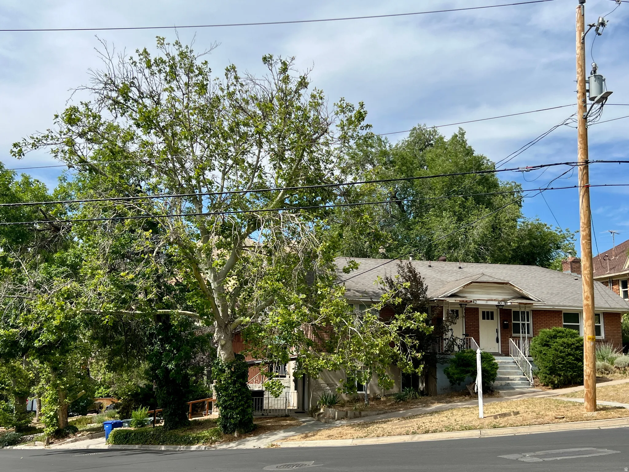 Single-story brick residence with a gabled entry porch, mature deciduous trees, and a sloped front yard