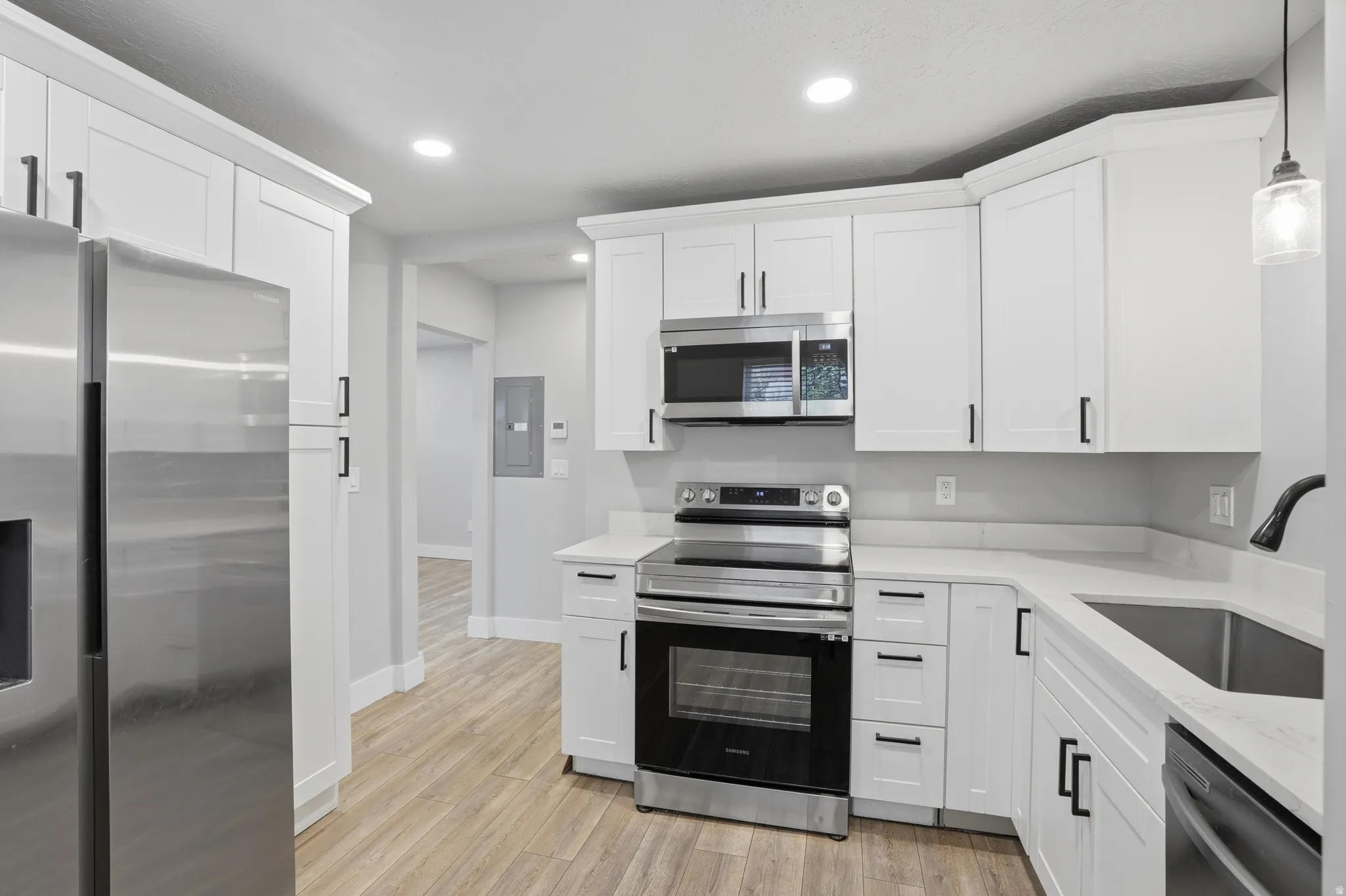Unit #40 Kitchen with stainless steel appliances, white cabinetry, light stone counters, light wood-type flooring, and pendant lighting