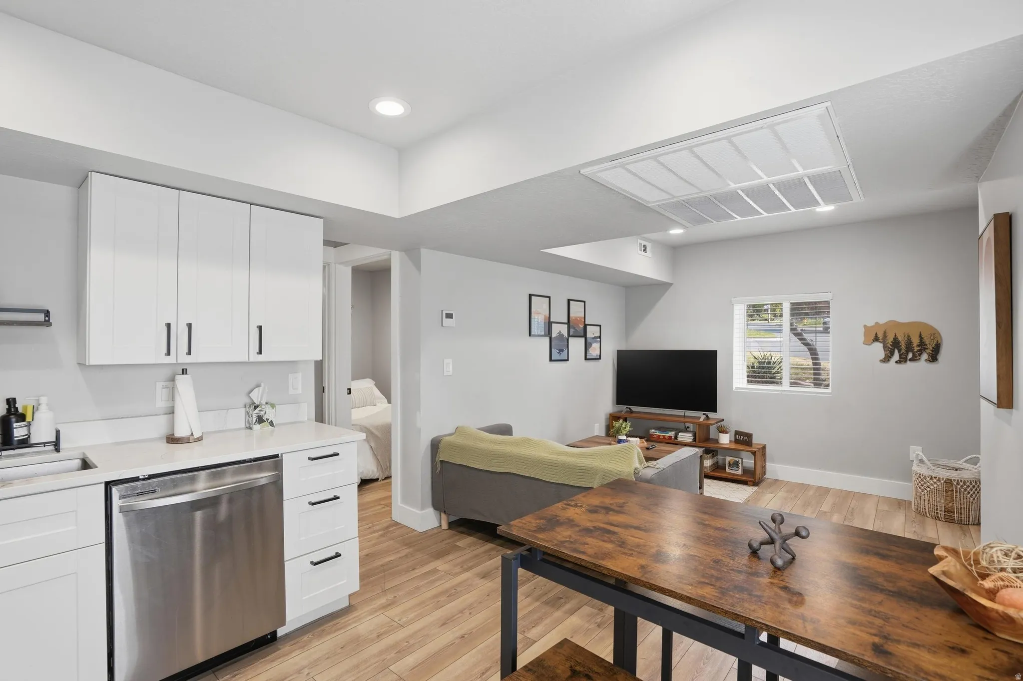 Furnished Unit #44 faces West. Kitchen with white cabinetry, stainless steel dishwasher, light wood-style floors, open floor plan, and recessed lighting
