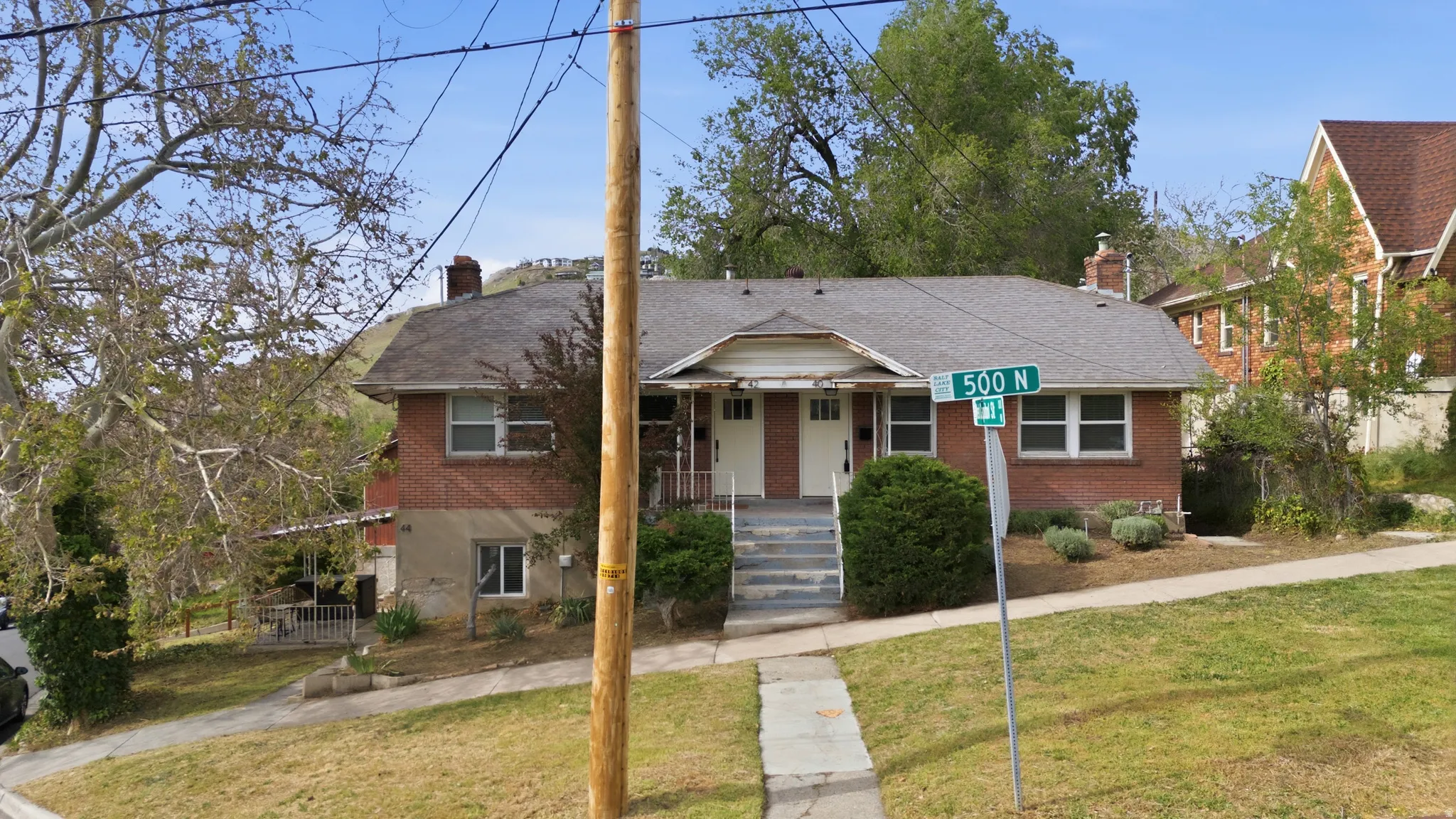 Bungalow-style Triplex house featuring a chimney, a front lawn, covered porch, brick siding, and a shingled roof