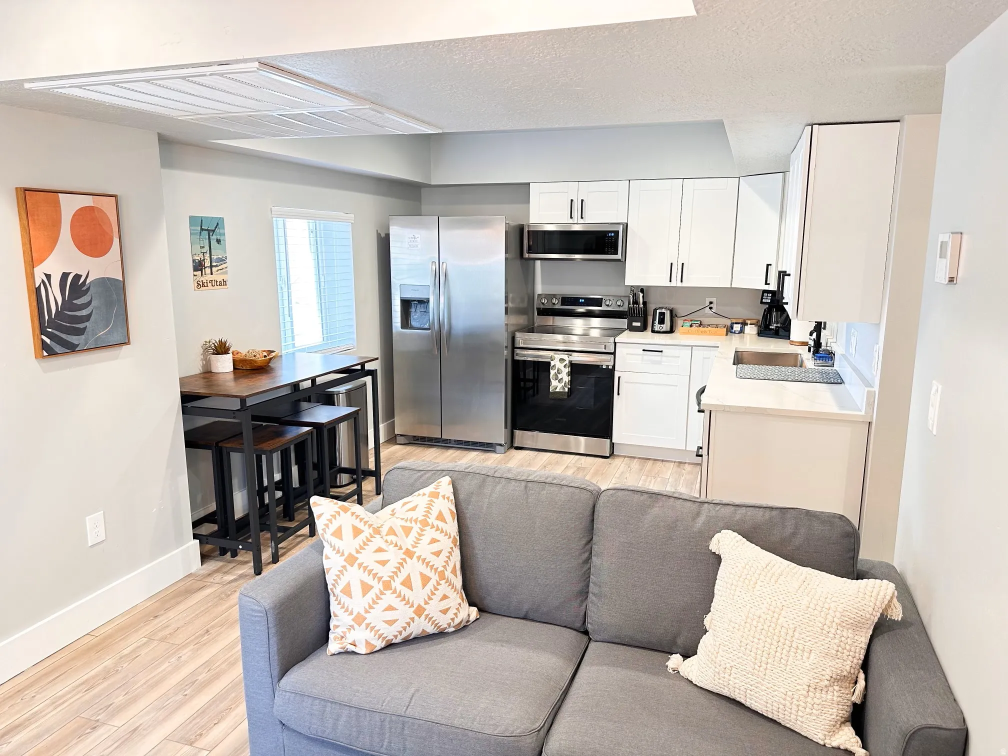 Furnished Unit #44 Kitchen featuring light wood-style floors, stainless steel appliances, white cabinets, a textured ceiling, and light stone counters