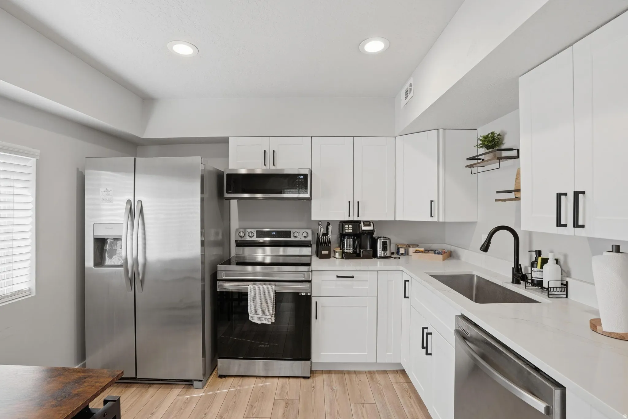 Furnished Unit #44 faces West. Kitchen with stainless steel appliances, light stone counters, white cabinets, and recessed lighting