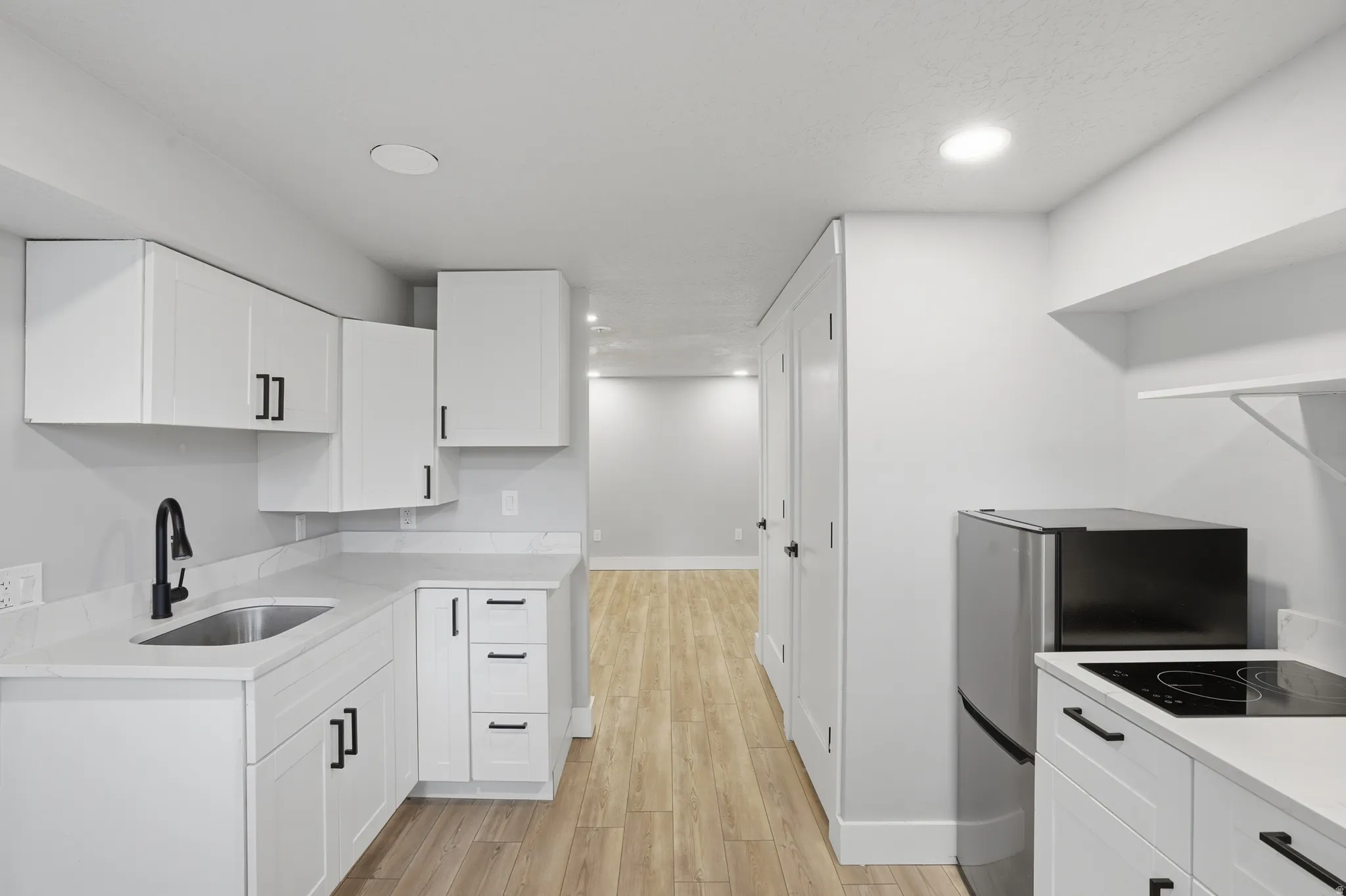 Unit #40 studio apartment with separate entrance.Kitchen featuring white cabinetry, light wood-style floors, recessed lighting, and black electric cooktop