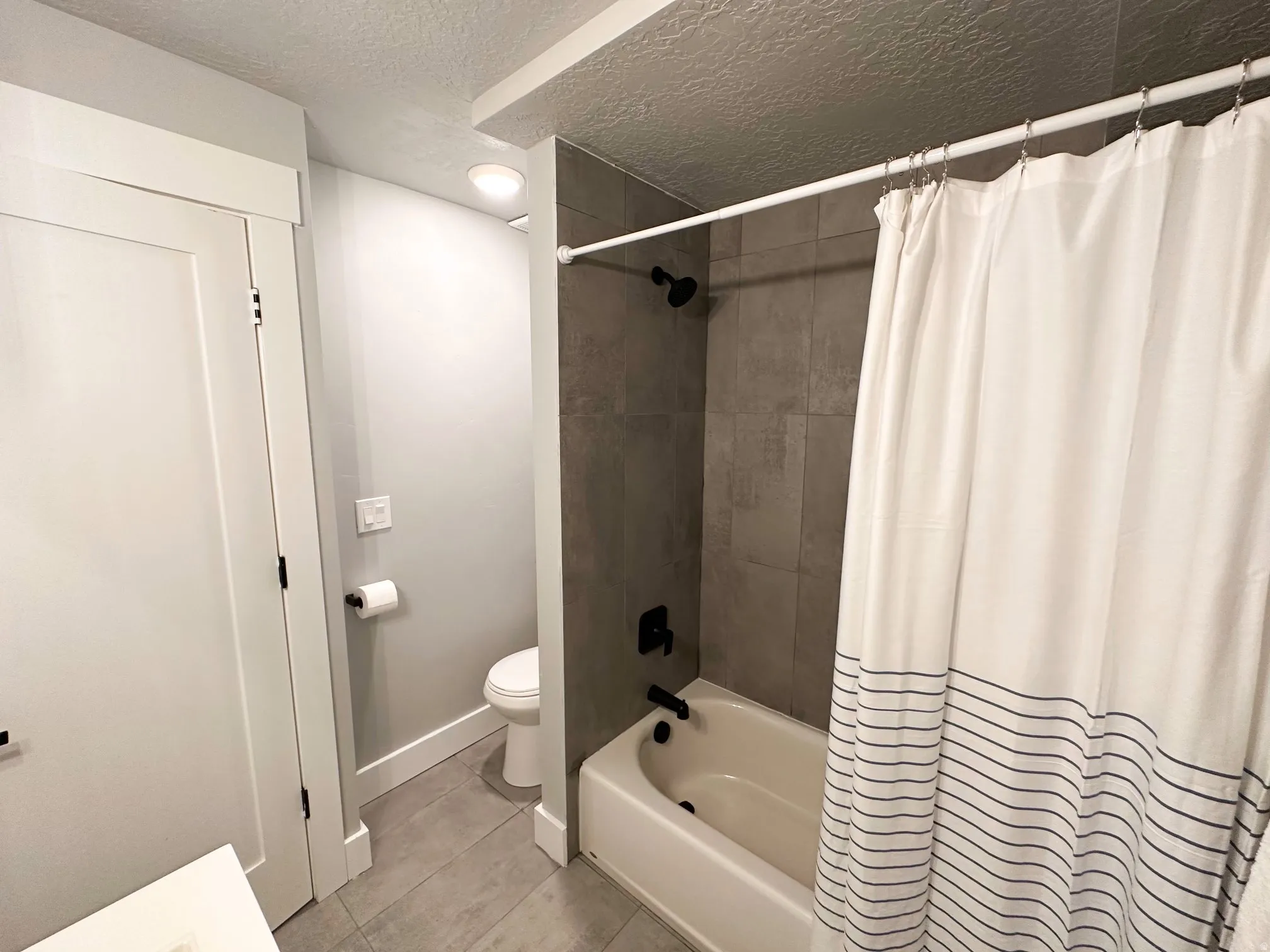 Furnished Unit #44 Full bathroom with a textured ceiling, shower / tub combo with curtain, and light tile patterned floors