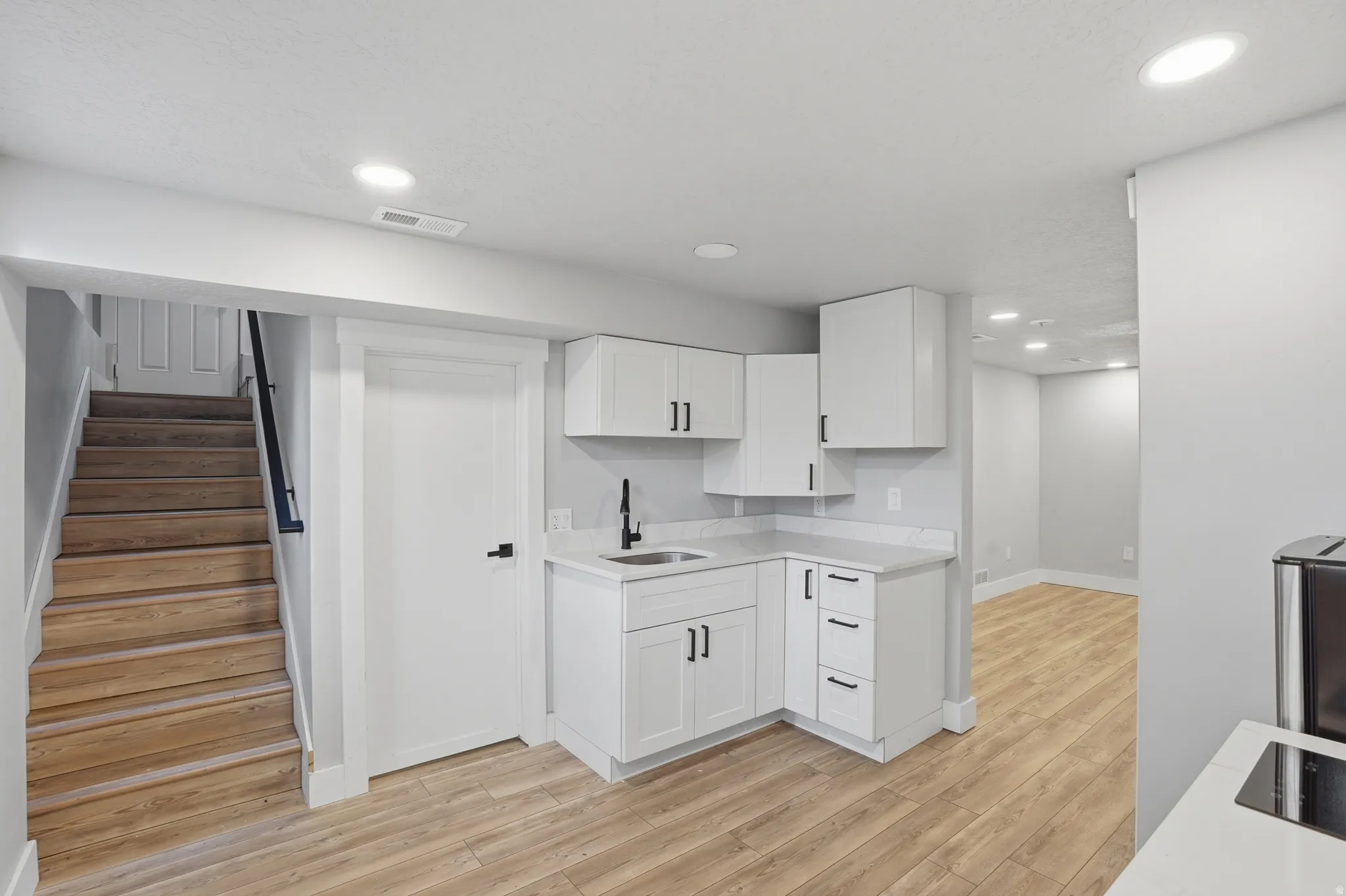 Unit #40 studio apartment with separate entrance. Kitchen with light wood-style floors, white cabinets, recessed lighting, and black electric stovetop
