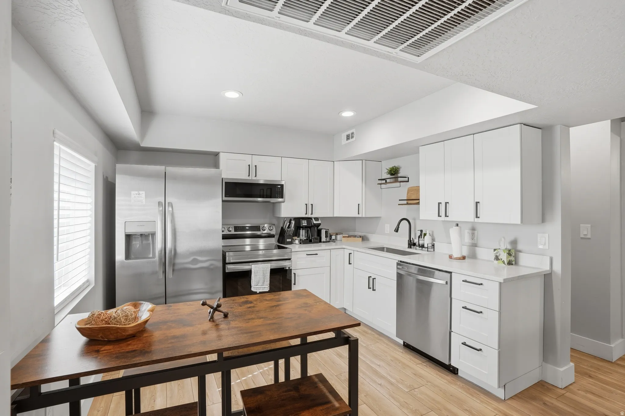 Furnished Unit #44 faces West. Kitchen with stainless steel appliances, white cabinetry, light wood-style floors, recessed lighting, and light stone counters
