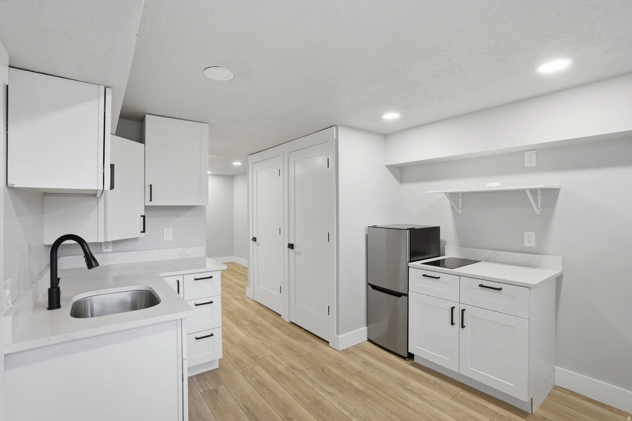 Unit #40 studio apartment with separate entrance.Kitchen featuring white cabinets, freestanding refrigerator, light wood finished floors, light stone counters, and recessed lighting