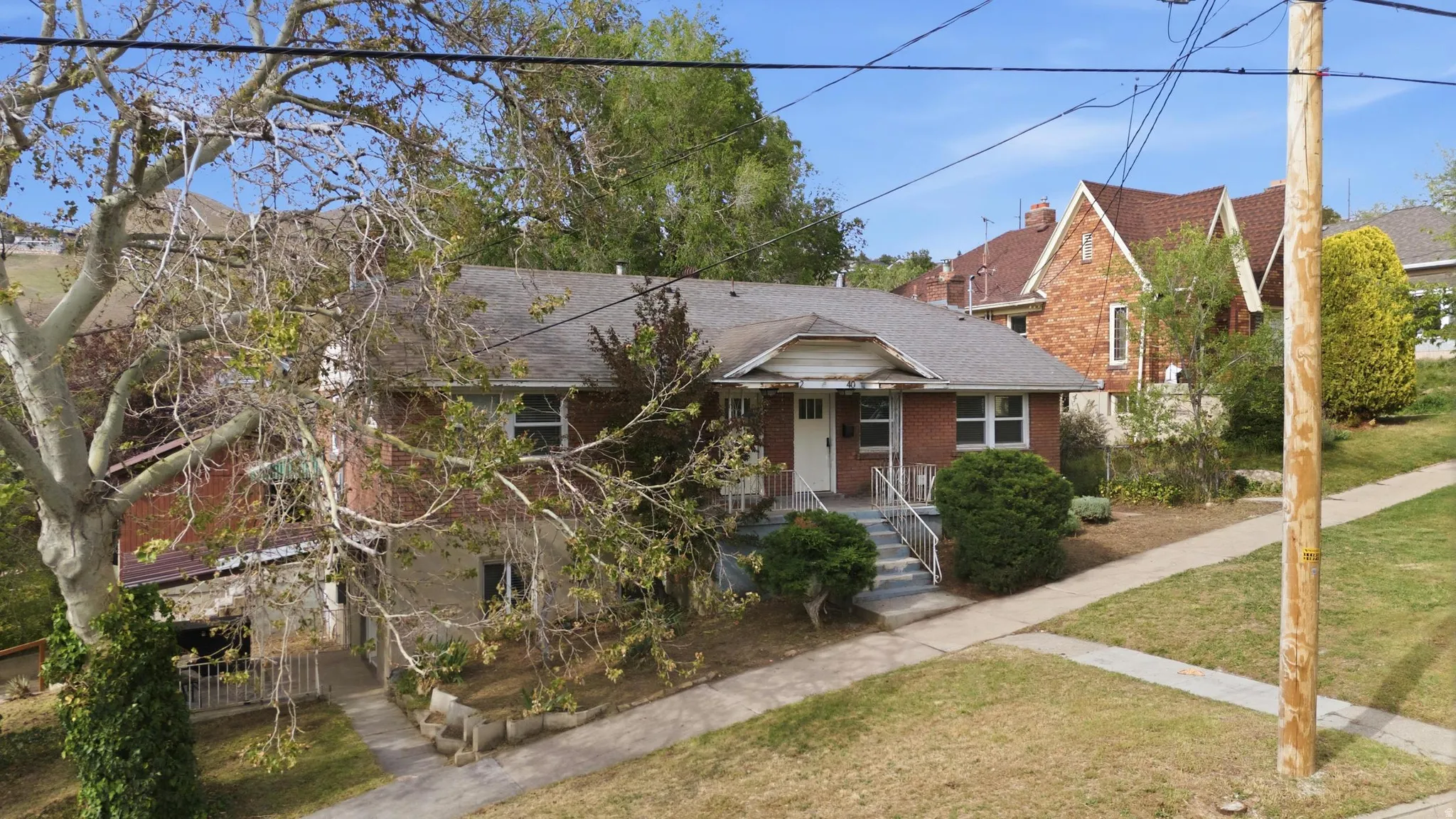 View of front of Triplex featuring a porch, brick siding, roof with shingles, and a front yard